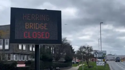 Andrew Turner/BBC A large sign at the side of a main road says 'Herring Bridge closed'.