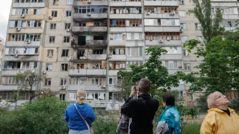 EPA-EFE Locals in the Ukrainian capital city Kyiv look up at a damaged apartment block following an attack by a Russia drone