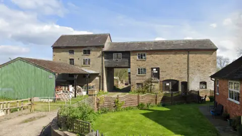 A old stone building made of a three-storey building connected to a four-storey building via a wooden-clad bridge