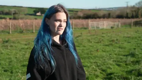 A woman with blue dyed hair looking to the site in a green field.