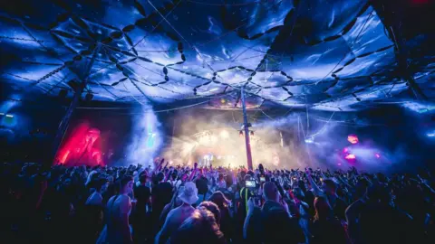 A crowd of people look towards a stage in an indoor venue 