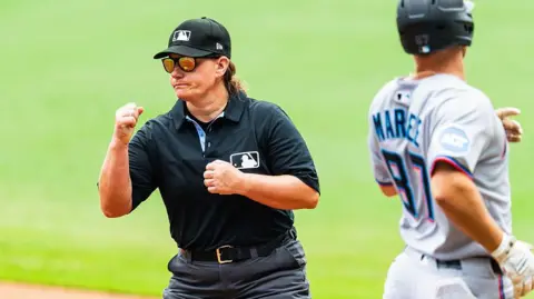 Getty Images An umpire wearing black does a hand signal to say that the baseball runner is out. 