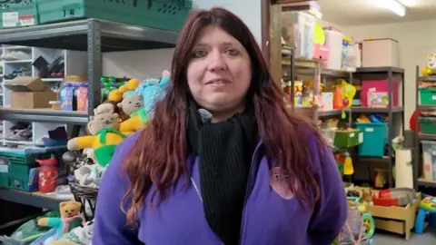 A woman with long brown hair smiling and stood in front of toys 