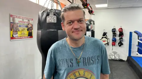 Chris Peskett stood in a boxing gym with a punch bag and a ring in the background