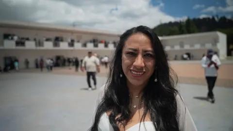 Ecuadorian voter Gabrila Kajo is for a picture next to a large open class in the background, which seems that people are casting their votes