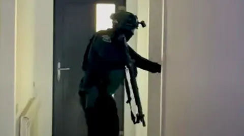 A screengrab from a video shows an armed police officer searching a house