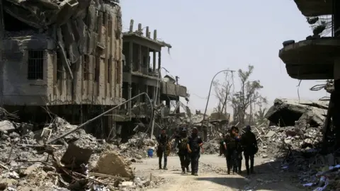 Reuters Iraqi security forces walk between destroyed buildings in the Old City of Mosul, Iraq (10 July 2017)
