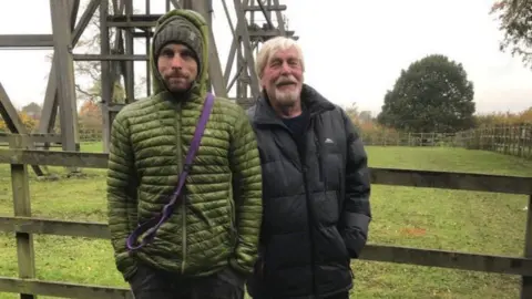 LDRS James Rogers and Alan Rogers stood in front of the wooden Brinsley Headstocks. James is in a green coat, while Alan is in a black coat.