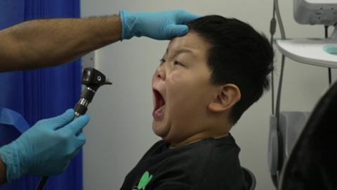 Child opens his mouth so a nurse can examine it