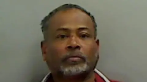 Mugshot of Nallathamby. He has short black hair and a white goatee beard.