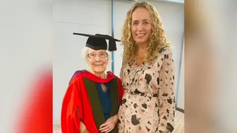 Michelle Rawlins Kathleen during a graduation ceremony when she was given an honorary degree in engineering by the University of Sheffield, wearing her ceremonial cap and gown. She is stood next to author Michelle Rawlins.