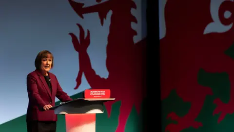 Getty Images Jo Stevens se encuentra en un podio rojo con una gran bandera de Gales colgada en la pared detrás de ella.