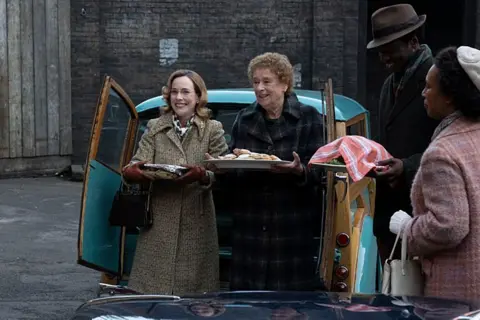 Perawat BBC/Neal Street Productions Shelagh Turner (Laura Main), Perawat Phyllis Crane (Linda Bassett) dan Cyril Robinson (Zephryn Taitte) membagikan makanan dari belakang mobil di East End