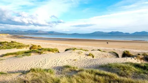 Getty Images Wide shot of Llanddwyn beach with mountains in the background and two people in the distance