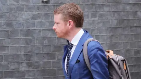 PA Media Morgan McSweeney wears a blue suit and brown backpack in a photo taken on 10 October 2024.