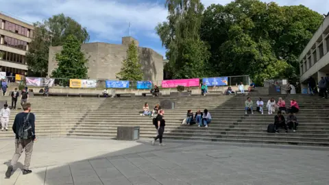 BBC Outside the university buildings, with a flight of curved concrete steps and students sitting on them in groups