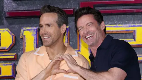 Getty Images Hugh Jackman and Ryan Reynolds smiling at a press event for Deadpool & Wolverine