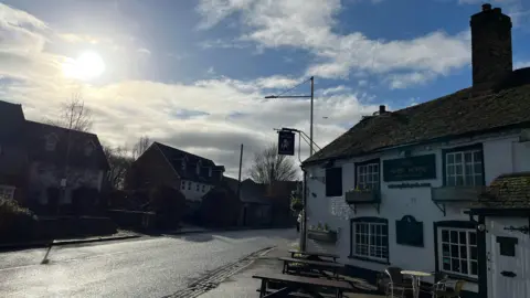 A old white building with benches outside with a road infront