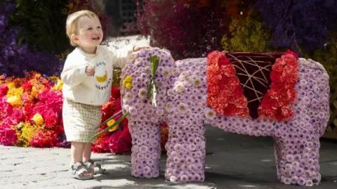 PA A toddler in shorts and sandals pats a floral pink elephant