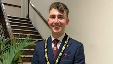 Harry Atkinson/Facebook Harry Atkinson stood in front of a staircase, dressed in a suit, smiling and wearing his mayoral chain