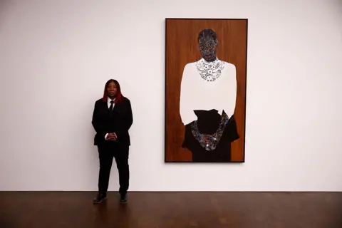 BENJAMIN CREMEL / AFP A woman dressed in a suit sands next to a portrait of  woman dressed in a white blouse and black skirt.