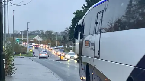 A large bus is next to a busy lane of traffic stretching far along the road.