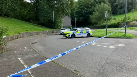 BBC The police cordon and cars on Cwm Road