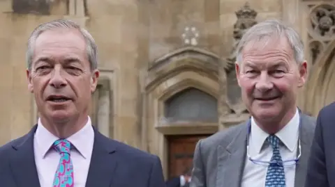 PA Media On the left is Nigel Farage who has grey hair, and is wearing a navy suit, with a pink shirt, and pink and blue tie. On the right is Rupert Lowe, who has grey hair, a grey suit jacket, white shirt, and blue tie. He has glasses around his neck. 