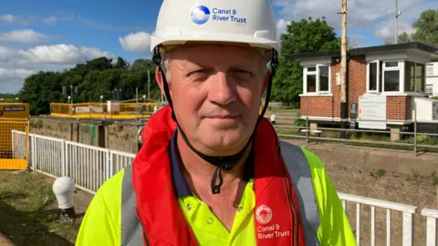 A man wearing a hard helmet and reflective clothing looks at the camera. 