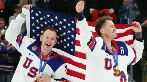 Brady Tkachuk and Matthew Tkachuk hold aloft the United States flag after helping the men's ice hockey team beat Canada to win gold at the 2026 Winter Olympics