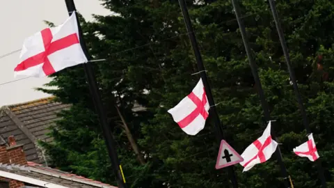 A row of four black lampposts with a small England flag tied to each.