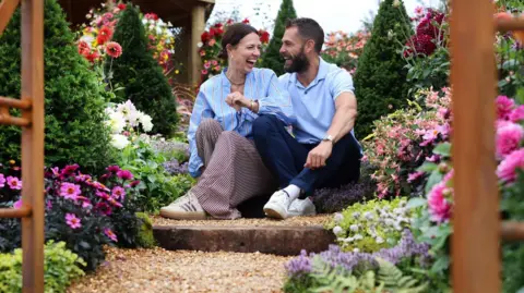 Gareth Jones Photography A couple pictured sitting on a step in a garden, laughing, surrounded by flowers.