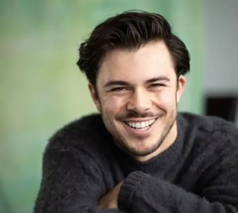 Jack Edwards Man with brown hair and wearing a grey jumper smiling at the camera