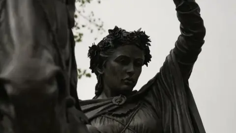 A close up of the lady's face against a grey sky. The horse is also on the shot.