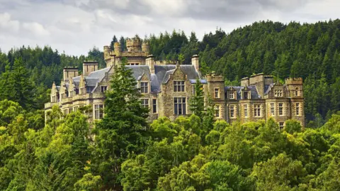 Getty Images Carbisdale Castle is a large property in Scottish baronial style. The top floors of the house rise above a heavily wooded area.
