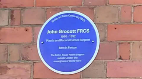 David Unwin A blue circular plaque with a white rim reads John Grocott FRCS 1910-1992 Plastic and Reconstructive Surgeon Born in Fenton , the first in-house Plastic Surgeon outside London and unsung hero of World War Two.