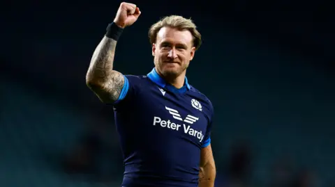 Reuters A man with blond hair in a Scotland rugby top raises his fist in the air in celebration