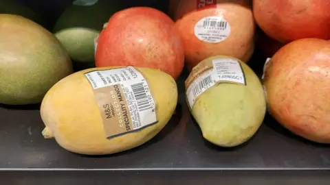 A Kesar mango on a shelf in Marks and Spencer with a small label that reads "speciality mango".