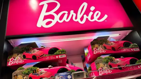 NurPhoto Barbie cars on display in a retail outlet. The white Barbie logo is above the toys on a hot pink background.