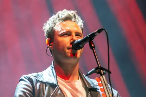 Getty Images A close-up image of Callum Beattie, in a leather biker jacket and white T-shirt, singing into a microphone during a performance.
