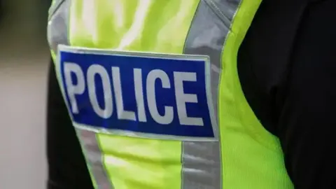 The back of police officer's fluorescent yellow vest. It has the word police written in white letters on a blue background