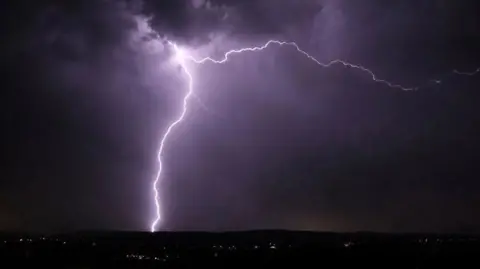 A bright shaft of lightning striking ground illuminates a dark night sky
