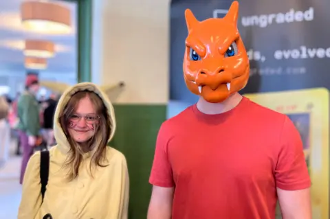 Jessica Jones-Shrigley is dressed in a yellow onesie with face paint and Daniel Stephenson is wearing a Charmander mask and orange t-shirt.