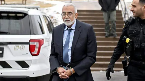 Getty Images Subramanyam “Subu” Vedam walks with handcuffs around his wrists