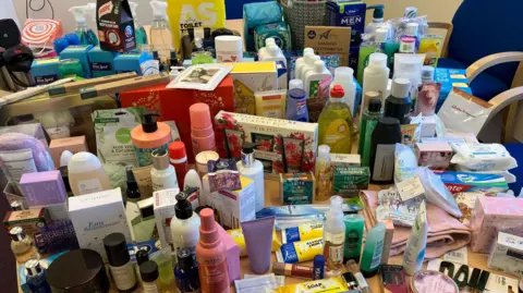 A table is covered with toiletry items, including shampoo, toothbrushes and cleaning products.