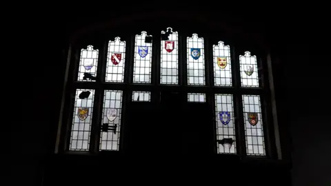 Qays Najm/BBC A large 13-panelled window with different stain-glass colour crests on the panes. 