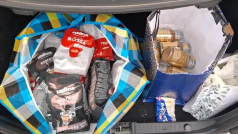 Cambridgeshire Police Two bags are in a boot of a car. The one on the left is full of coffee bags and the one on the right is half full with coffee jars.