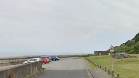 A general view of the area where the skate park will be built. It shows the promenade with cars park along it and a building on the other side of the road