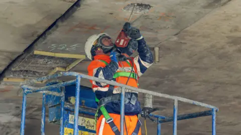 Newcastle Council A workman is stood in a cherry-picker and drilling into the underneath of a concrete flyover.
