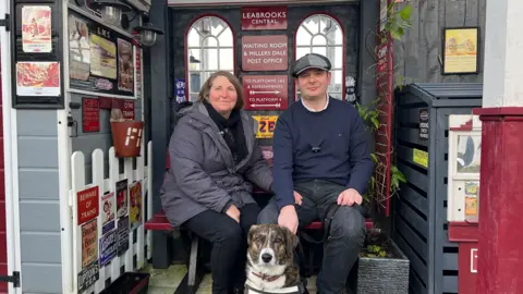 Katherine Siggins and Richard Cantrell sat in their back garden in Leabrooks, where the couple have created a model railway platform decorated with signs and model trains.